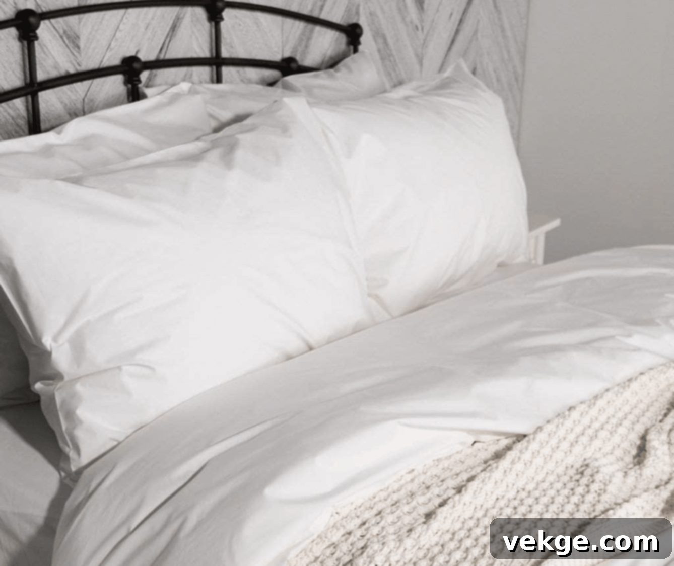 Close-up of a bed with crisp white percale sheets and layered bedding in a farmhouse style bedroom.