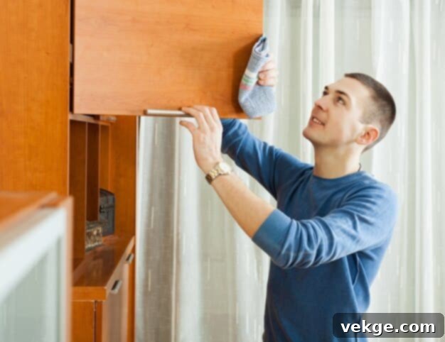 Man cleaning wooden kitchen cabinets with a soft cloth