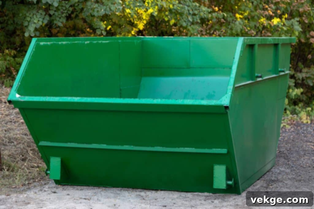 Empty large green metal construction dumpster against a background of trees.