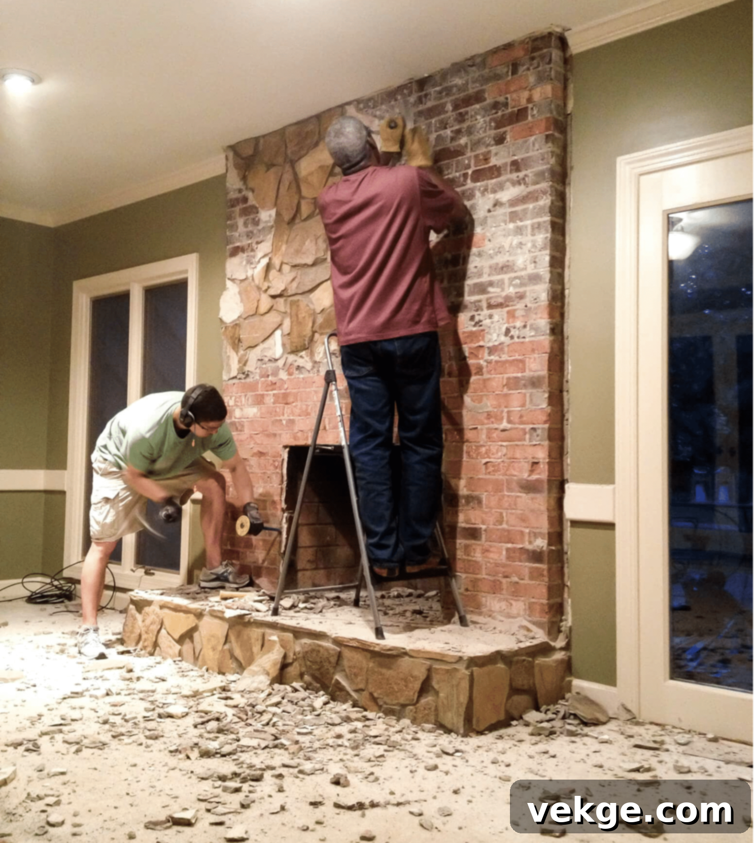 Using a demolition hammer to remove an old stone fireplace facade, revealing brick underneath.