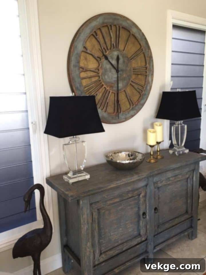 A large, rustic wooden wall clock with Roman numerals hangs prominently on a textured white wall, acting as a stylish focal point in a modern farmhouse-inspired room.