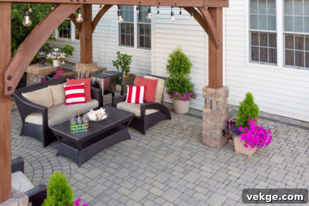 Comfortable chairs with colorful red cushions on an outdoor brick patio covered by a wooden gazebo in front of a timber clad house