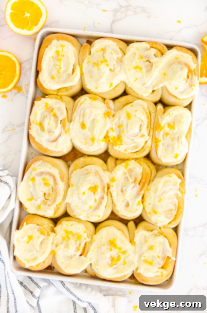 Sweet Orange Swirls 8 A close-up shot of a single orange roll, heavily glazed, with visible orange zest and soft texture.