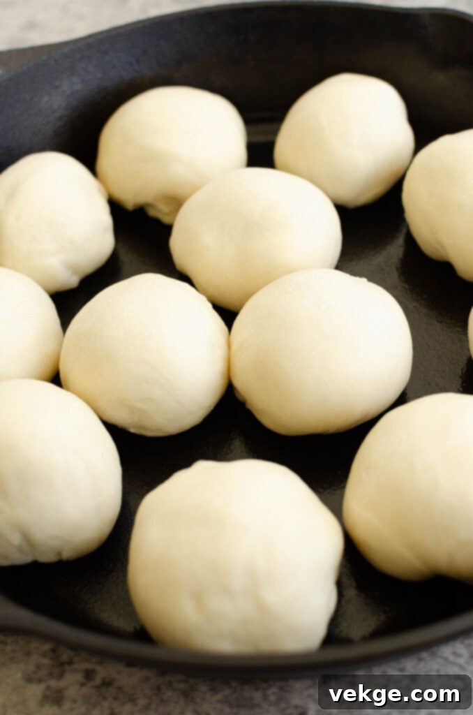 A baker shaping dough into individual rolls on a floured surface.