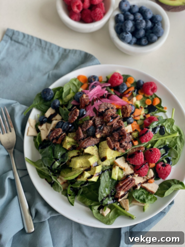 A vibrant and colorful Spinach Berry Salad with chicken, berries, and nuts, drizzled with dressing.