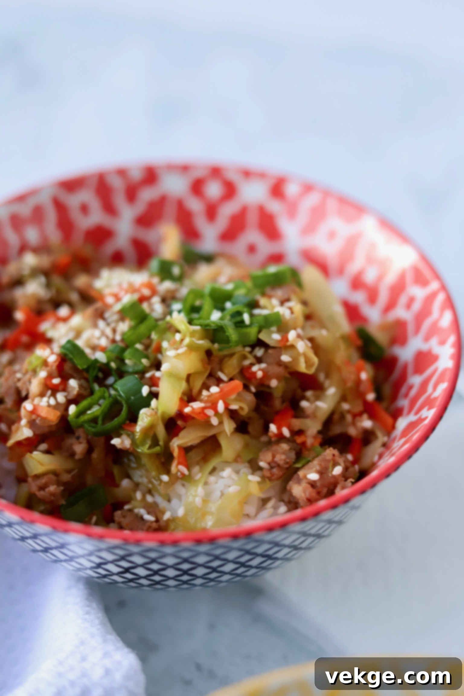 A vibrant and delicious Egg Roll in a Bowl, served over a bed of rice with fresh green onions and sesame seeds for garnish.
