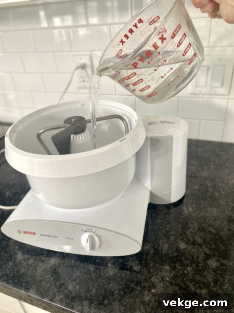 Artisan Sourdough Burger Buns 9 Water being poured into a bowl with flour, emphasizing the hydration step in dough making.