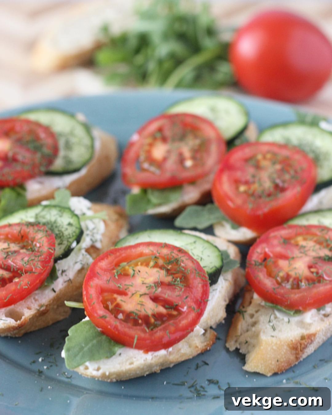 Close-up of a single baguette bite showing the layers of cream cheese, cucumber, tomato, arugula, and dill.