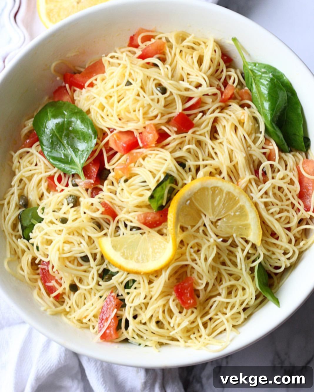 Close-up of freshly cooked capellini pasta mixed with the lemon dressing, capers, and chopped tomatoes, ready for chilling.