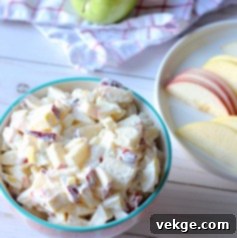 Close-up view of fresh, colorful diced apples being gently mixed into a rich, white creamy dressing.