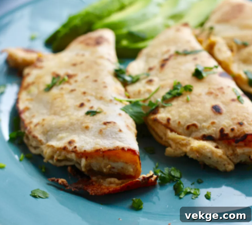 A close-up of a perfectly baked, golden-brown chicken taquito with a peek of creamy filling, alongside a small dish of guacamole.