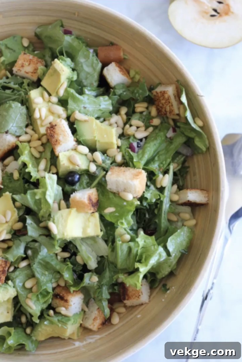 An overhead view of the Sweet and Savory Green Salad, neatly arranged in a bowl with all its colorful ingredients visible: various greens, crispy bacon bits, diced avocado, pine nuts, goat cheese crumbles, and slices of apple.