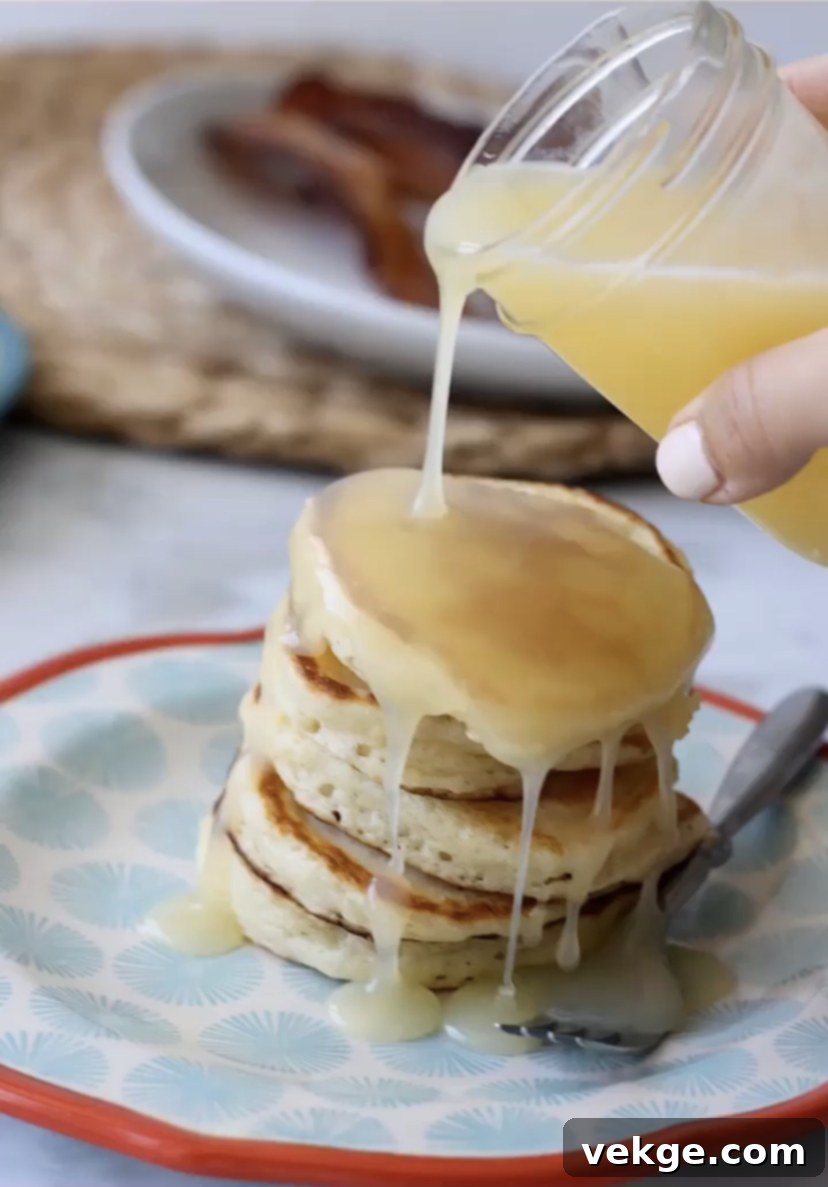 A stack of golden buttermilk pancakes topped with creamy syrup, resting on a white plate with a side of fresh berries.