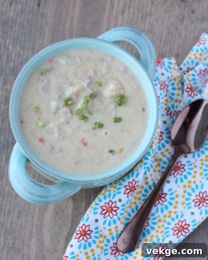A steaming bowl of creamy ham and potato soup, garnished with fresh herbs, against a cozy winter backdrop.